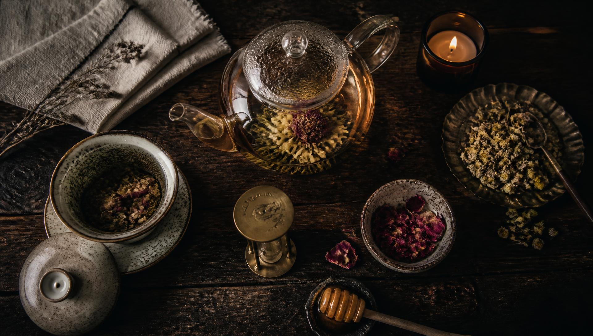 A kettle pouring hot water over loose leaf tea in a glass teapot on a wooden table